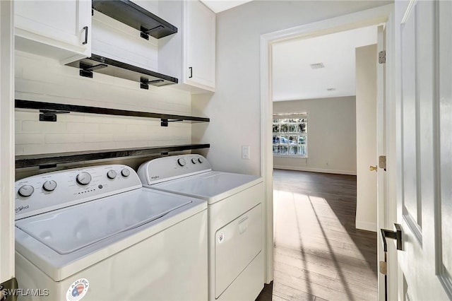 laundry area with washing machine and clothes dryer, cabinet space, visible vents, wood finished floors, and baseboards