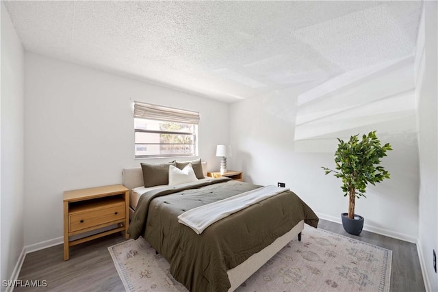 bedroom featuring a textured ceiling, baseboards, and wood finished floors