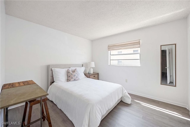 bedroom with a textured ceiling, wood finished floors, and baseboards