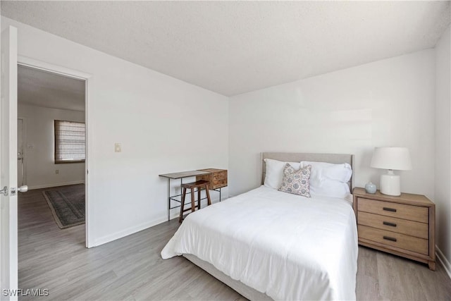 bedroom with light wood-style floors, baseboards, and a textured ceiling