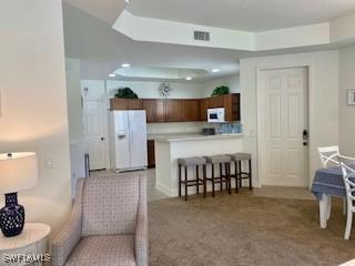 kitchen with a breakfast bar, a tray ceiling, light countertops, white appliances, and a peninsula