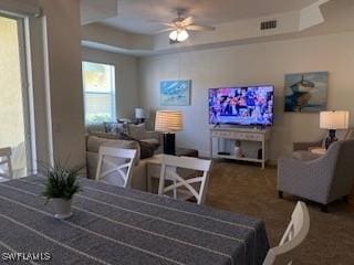 carpeted dining space featuring ceiling fan, visible vents, and a raised ceiling