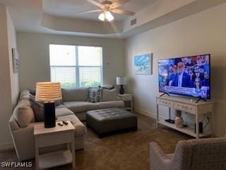 carpeted living room with visible vents, a tray ceiling, a ceiling fan, and baseboards