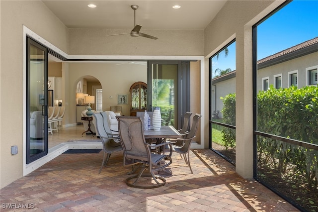 sunroom with arched walkways and a ceiling fan