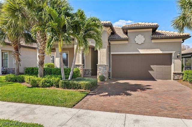 mediterranean / spanish home featuring a garage, a tile roof, stone siding, decorative driveway, and stucco siding