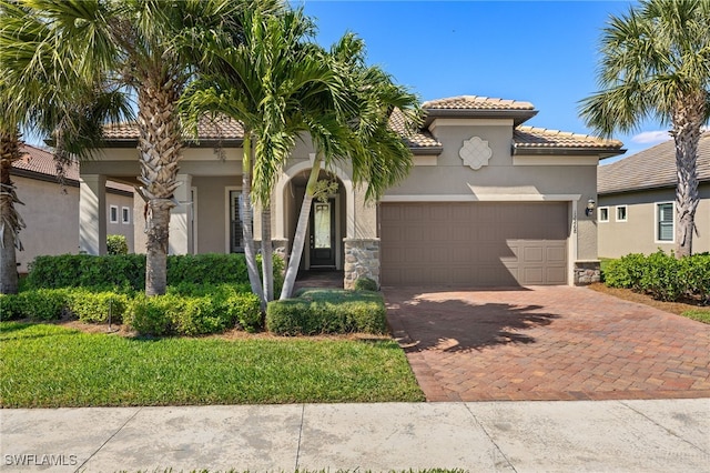 mediterranean / spanish-style home featuring a garage, a tiled roof, stone siding, decorative driveway, and stucco siding