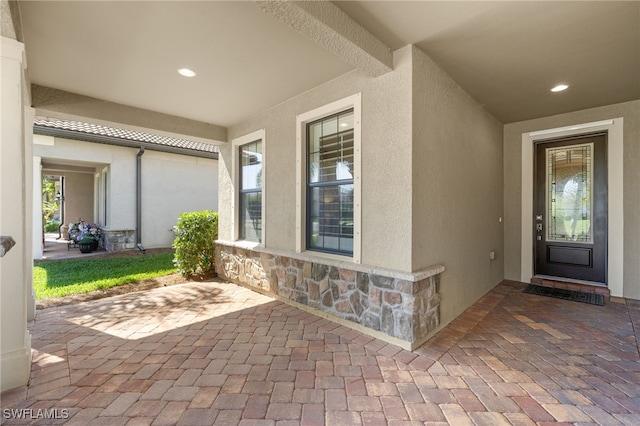 entrance to property featuring stone siding, a patio, and stucco siding