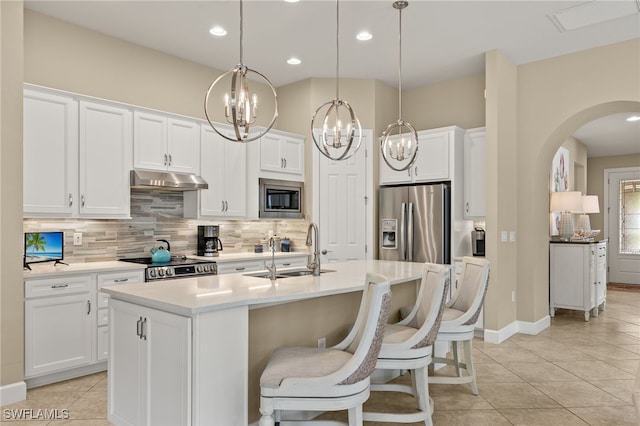 kitchen featuring stainless steel appliances, decorative backsplash, white cabinets, a sink, and under cabinet range hood