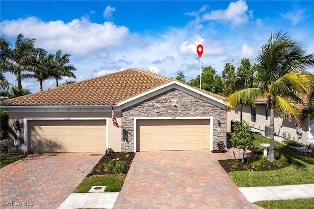 view of front facade featuring driveway, stone siding, a tile roof, and stucco siding