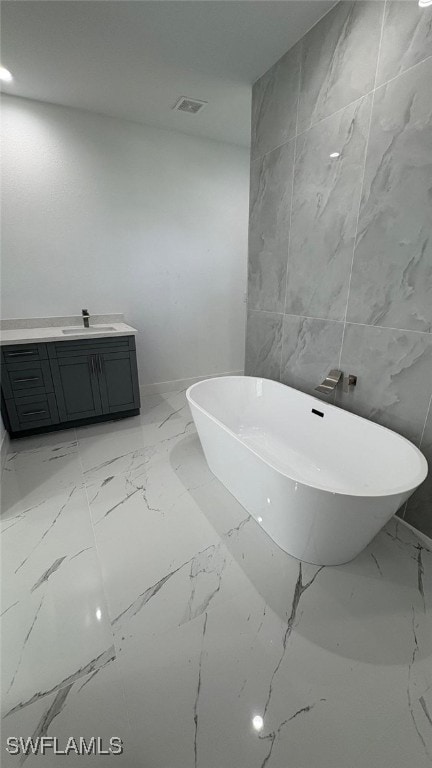 full bathroom featuring visible vents, marble finish floor, a freestanding bath, vanity, and stone wall