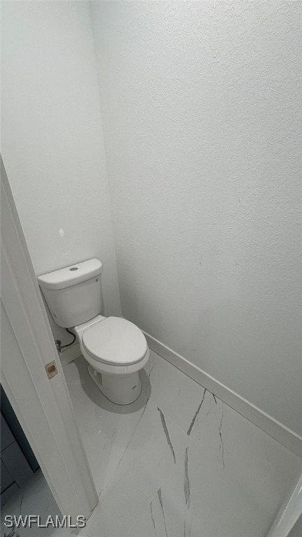 bathroom featuring toilet, marble finish floor, and baseboards