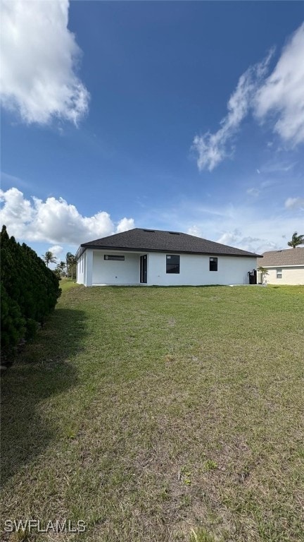 rear view of house featuring a yard and stucco siding