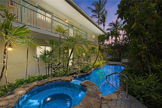 pool at dusk with a pool with connected hot tub