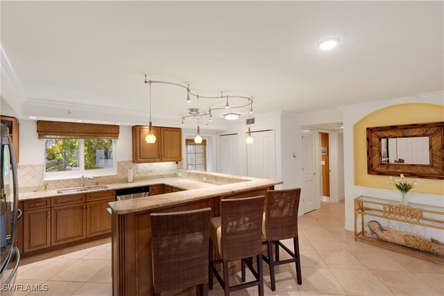 445 3rd Ave S Unit 102, Naples, FL 34102 - kitchen featuring a breakfast bar area, light tile patterned floors, brown cabinets, and ornamental molding
