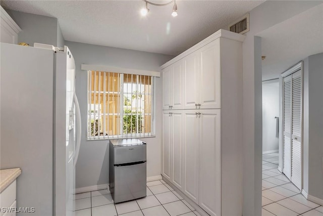 kitchen featuring light tile patterned floors, visible vents, freestanding refrigerator, white cabinets, and white refrigerator with ice dispenser