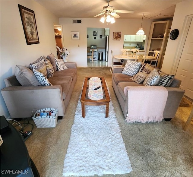 living area featuring ceiling fan, visible vents, and light colored carpet