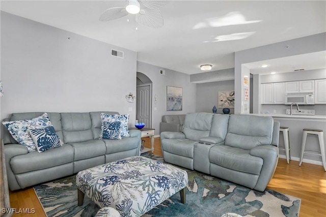 living area with arched walkways, light wood-style floors, visible vents, and a ceiling fan