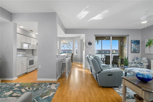 living area featuring baseboards, a ceiling fan, and light wood-style flooring
