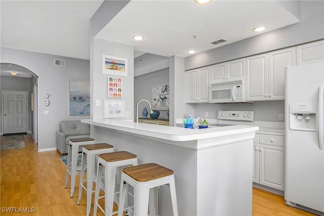 kitchen featuring a kitchen breakfast bar, light countertops, visible vents, white appliances, and arched walkways