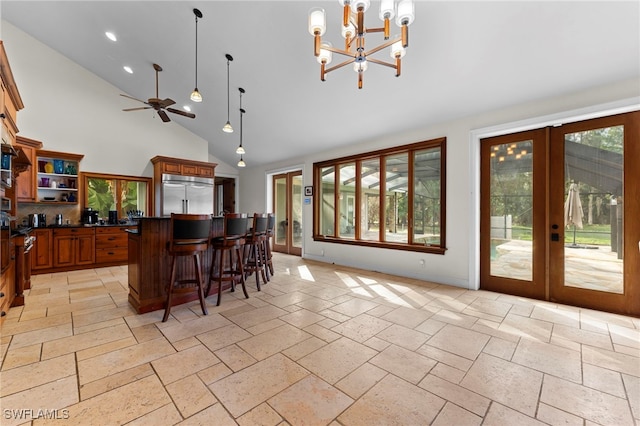 kitchen featuring a breakfast bar, decorative light fixtures, dark countertops, stone tile flooring, and stainless steel built in refrigerator