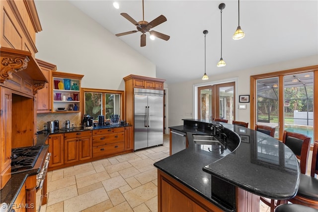 kitchen featuring a breakfast bar area, open shelves, hanging light fixtures, appliances with stainless steel finishes, and a kitchen island with sink