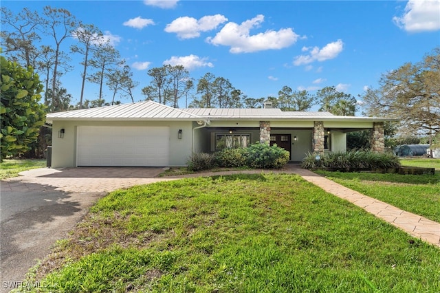 single story home with a front yard, metal roof, a garage, stone siding, and driveway