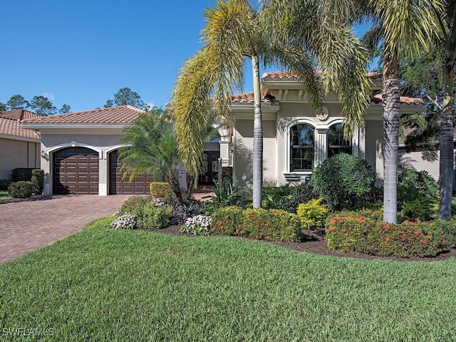 mediterranean / spanish house featuring a garage, a tile roof, decorative driveway, stucco siding, and a front yard