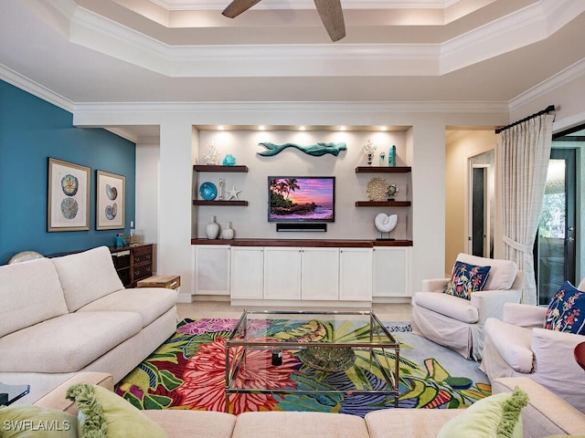 living area with ceiling fan, a tray ceiling, and crown molding