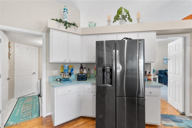 kitchen featuring light wood-type flooring, light countertops, stainless steel fridge, and white cabinetry