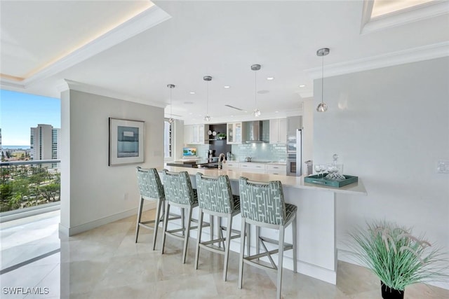 kitchen with a peninsula, light countertops, wall chimney range hood, backsplash, and crown molding