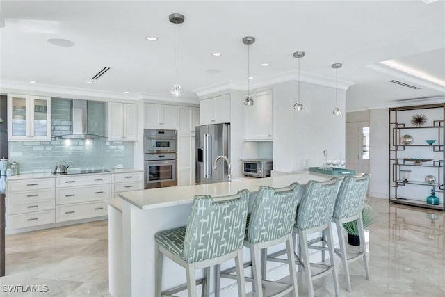 kitchen featuring visible vents, appliances with stainless steel finishes, white cabinetry, wall chimney range hood, and a peninsula