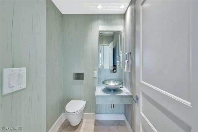 half bath featuring marble finish floor, vanity, toilet, and baseboards