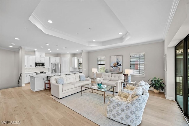 living room with light wood finished floors, ornamental molding, a raised ceiling, and recessed lighting