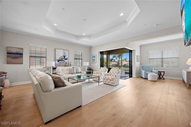 living room featuring light wood-type flooring, a tray ceiling, a healthy amount of sunlight, and crown molding