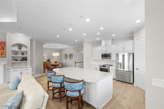 kitchen featuring light wood finished floors, a kitchen island, ornamental molding, stainless steel appliances, and white cabinetry