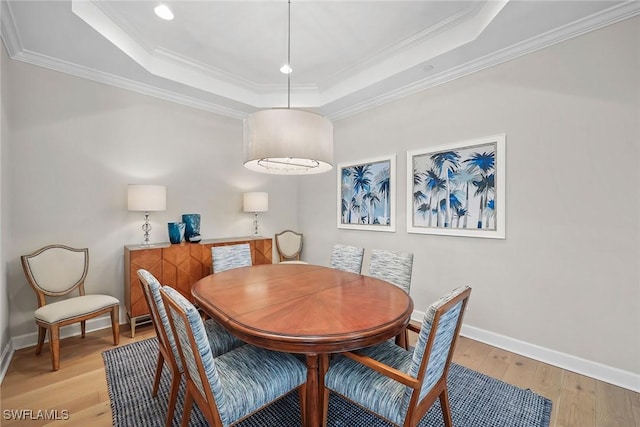 dining area with baseboards, a raised ceiling, light wood-style flooring, and crown molding