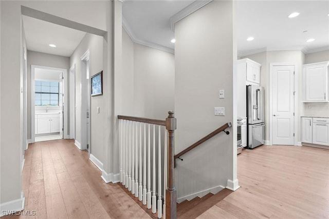 hallway featuring ornamental molding, light wood-style flooring, an upstairs landing, and baseboards