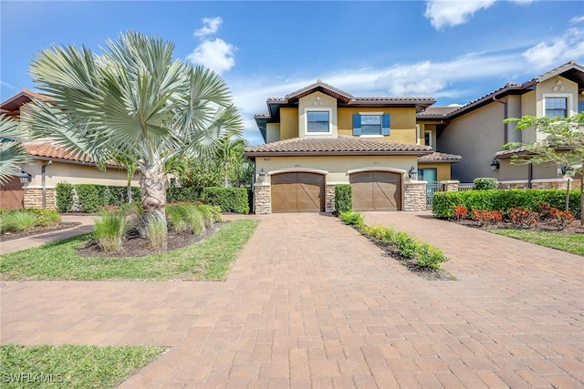 mediterranean / spanish-style home with decorative driveway, a tile roof, stucco siding, an attached garage, and stone siding