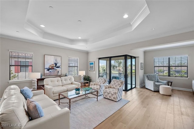 living area featuring ornamental molding, a wealth of natural light, a raised ceiling, and light wood-style flooring