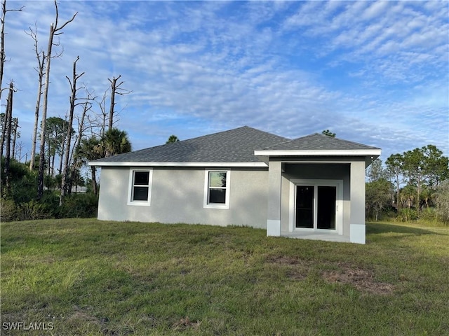 rear view of house featuring stucco siding, a shingled roof, and a yard