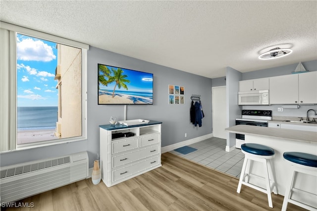 kitchen with white appliances, a breakfast bar, white cabinetry, light countertops, and light wood finished floors