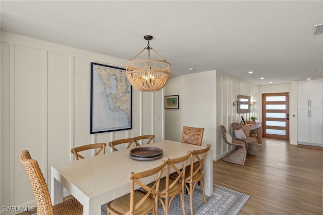 dining space with recessed lighting, a decorative wall, wood finished floors, visible vents, and an inviting chandelier