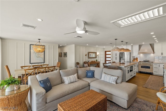 living room featuring recessed lighting, wood finished floors, visible vents, and a decorative wall