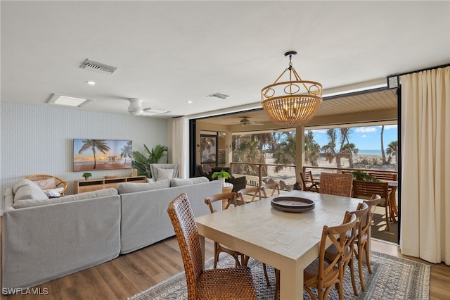 dining area featuring ceiling fan with notable chandelier, wood finished floors, visible vents, and wallpapered walls