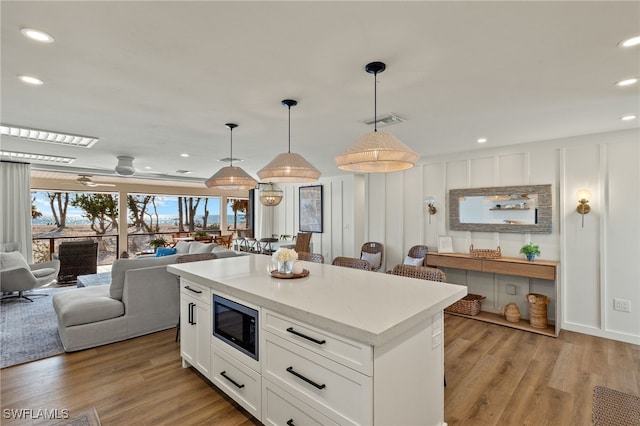 kitchen featuring decorative light fixtures, light countertops, open floor plan, white cabinetry, and built in microwave