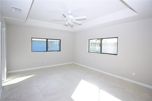 unfurnished room with visible vents, baseboards, ceiling fan, a tray ceiling, and light tile patterned flooring