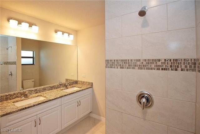 bathroom featuring toilet, double vanity, a tile shower, and a sink