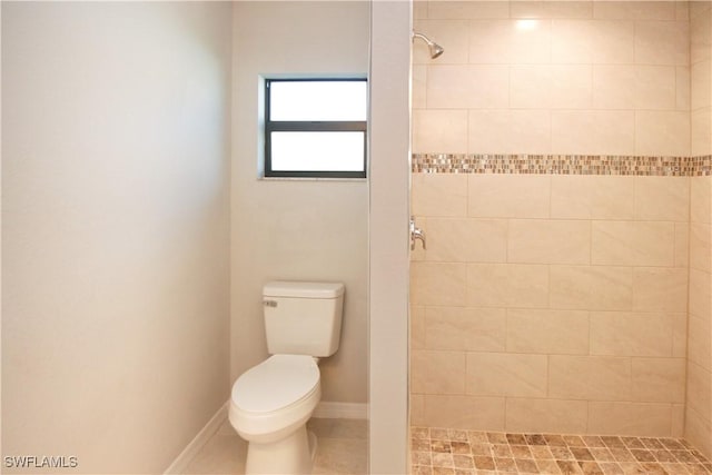 bathroom with toilet, baseboards, tiled shower, and tile patterned floors