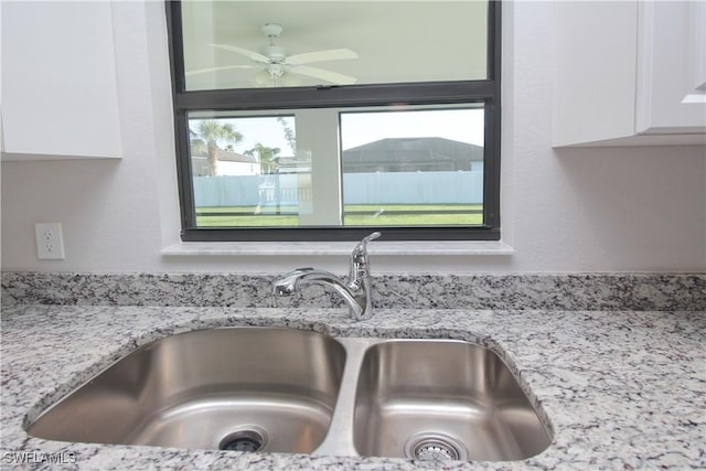 details with ceiling fan, white cabinets, a sink, and light stone countertops