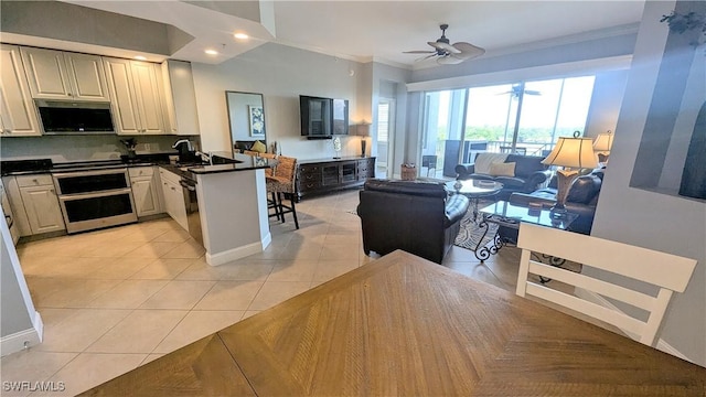 kitchen with light tile patterned floors, stainless steel microwave, open floor plan, oven, and a peninsula